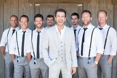 a group of men standing next to each other in front of a wooden door wearing white suits and black ties