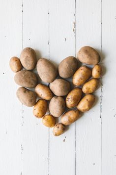 potatoes arranged in the shape of a heart on a white wooden background, top view