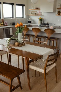 a kitchen table and chairs with flowers in a vase on the dining room table next to it