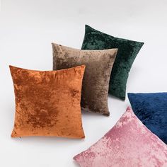 four different colored velvet pillows on a white surface