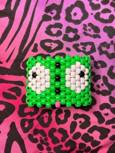 a green and white beaded brooch sitting on top of a leopard print fabric