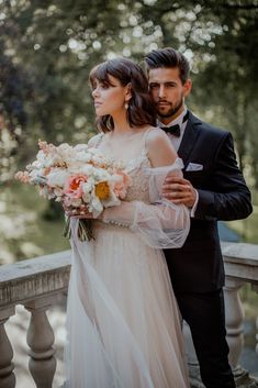 a bride and groom standing on a balcony holding bouquets of flowers in their hands