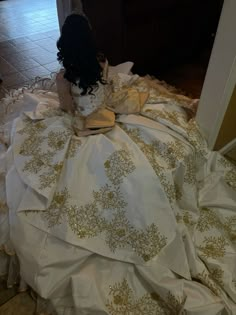 a doll sitting on top of a bed covered in white and gold cloths,