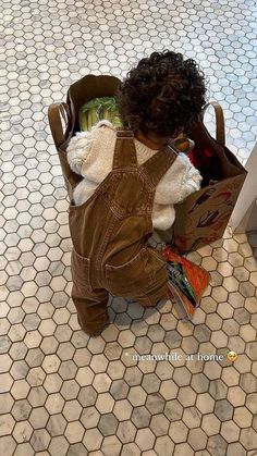 a toddler sitting in a bag on the floor with a stuffed animal inside it