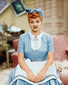 a woman with red hair sitting on a chair in a blue and white checkered dress