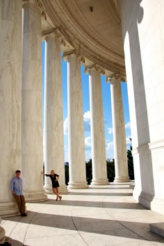 a man and woman standing in front of some white pillars with columns on each side