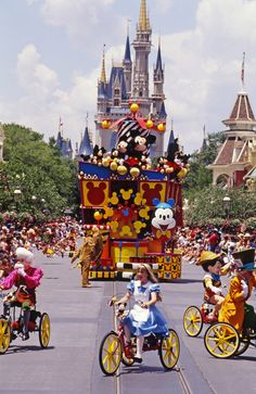 several people riding bicycles in front of a float with mickey mouse on it's back