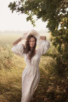 a woman in a white dress and hat is posing for the camera with her hands on her head