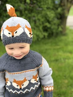 a little boy wearing a knitted sweater and hat with foxes on it's back