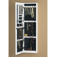 a white wall mounted jewelry cabinet with multiple necklaces and bracelets hanging on it