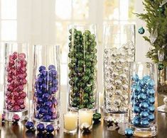 several vases filled with balls and candles on a table next to a christmas tree