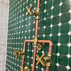 a green tiled wall with brass pipes and cross handles