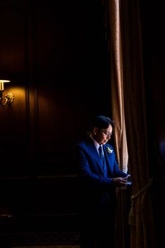 a man in a blue suit standing next to a window looking at his cell phone