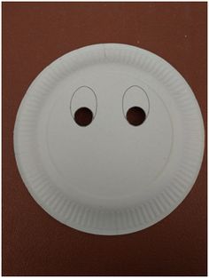 a white paper plate with two eyes and one eye drawn on the side, sitting on a brown surface