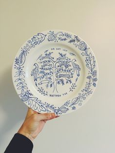 a hand holding a blue and white plate with an image of a tree on it