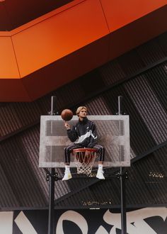 a man sitting on top of a basketball hoop with a basketball in his hand while holding a basketball