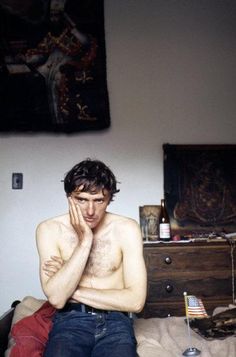 a shirtless man sitting on top of a bed in front of a dresser with his hands to his face