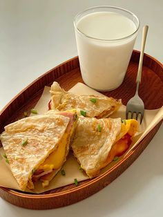 two quesadillas and a glass of milk on a wooden tray with utensils