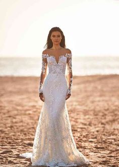 a woman standing on top of a sandy beach wearing a wedding dress with long sleeves