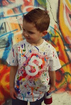 a young boy standing in front of graffiti covered wall