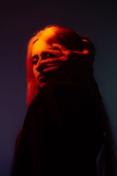 a woman with red hair covering her face and hand over her mouth, against a dark background