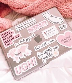 a laptop computer covered in stickers on top of a white bed next to a pink teddy bear