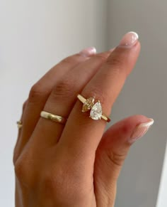 a woman's hand holding a gold ring with a pear shaped diamond on it