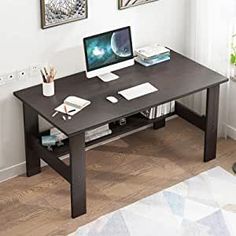 a desk with a computer on top of it in front of two pictures hanging on the wall