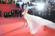 a woman in a long white dress standing on a red carpet with photographers behind her