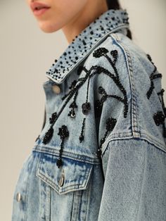 a woman wearing a jean jacket with black beads on it