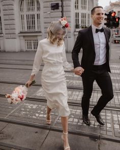 a bride and groom walking down the street holding hands