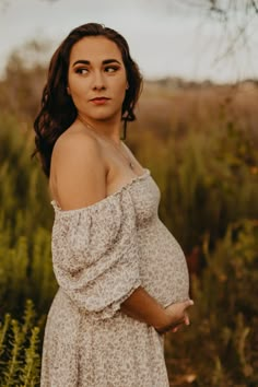 a pregnant woman standing in a field with her hands on her hips and looking at the camera