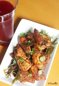 a white plate topped with chicken wings next to a glass of juice