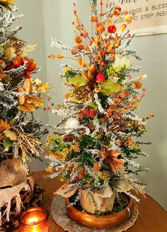 two christmas trees decorated with orange and white flowers on top of a wooden table next to candles