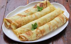 three crepes on a white plate sitting on a wooden table