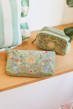 two green bags sitting on top of a wooden table next to a pillow and plant