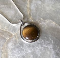 This petite pendant features a lovely, natural, Tiger's eye gemstone. I chose this gemstone because I have always been drawn to its energy and had yet to work with it!  I loved the movement in the stone, and wanted to keep the setting simple but unique. I started with a pure silver, serrated, bezel wire, to secure the stone. Then I created a sterling silver platform to reveal the back of the stone, while securing it. Then, I created a pear shape with think sterling silver wire. I placed the Tiger eye inside, and soldered it to the bottom right side of the shape. I used a lined and dimpled pattern on the bale to add texture and reinforce the modern look.  The bale is about 5mm, allowing for a variety of chains to comfortably be threaded through!  Since I was a child, I have been drawn to Ti Bezel Wire, Eye Meaning, Silver Platforms, Tiger Eye Crystal, Tigers Eye Necklace, Tigers Eye Gemstone, Snake Chain, Tiger Eye, Pure Silver