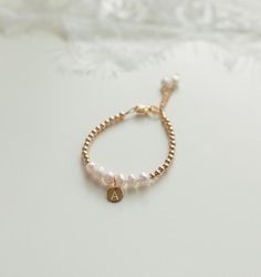 a gold bracelet with white pearls and a small charm on the clasp is sitting on a table