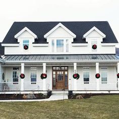 a large white house with wreaths on the front porch and two red christmas wreaths hanging from the roof