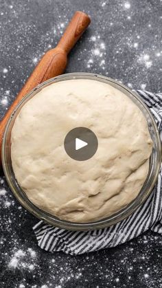 a bowl filled with dough sitting on top of a table next to a wooden spoon