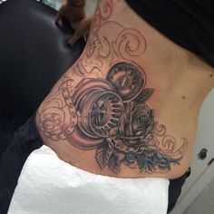 a woman's stomach with a clock and roses tattoo on her side ribcage