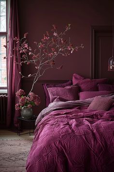 a bed with purple sheets and pillows in a room next to a vase filled with flowers