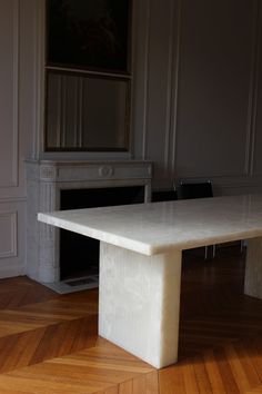 a white marble table sitting on top of a wooden floor next to a fire place