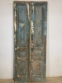 an old wooden door with peeling paint on the doors and bottom panel is open to reveal a white wall