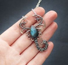 a hand holding a silver necklace with a blue stone in the shape of an octopus