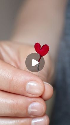 a person holding a heart shaped pin with a video playing button in the middle of their thumb