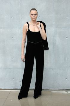 a woman standing in front of a concrete wall wearing black velvet jumpsuits and a crop top