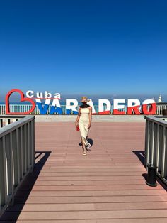 a woman walking across a wooden bridge with a sign in the background that reads cura radero