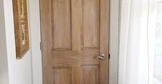 a wooden door in the corner of a room next to a window with white curtains