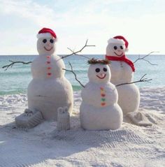 three snowmen sitting in the sand at the beach